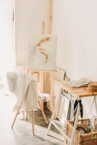 Cozy artist studio with bright lighting, an easel displaying a canvas, and a chair.